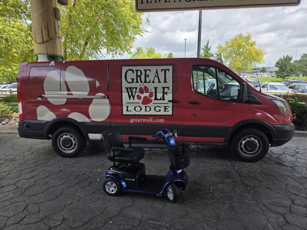 Mobility Scooter Parked in front of a van with advertisement for Great Wolf Lodge