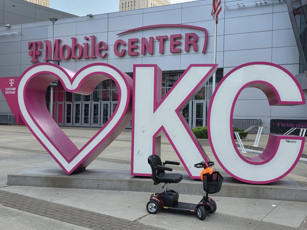 Mobility Scooter In Front of a large display with a Heart and the Letters K and C. The T-Mobile Center is in the background.