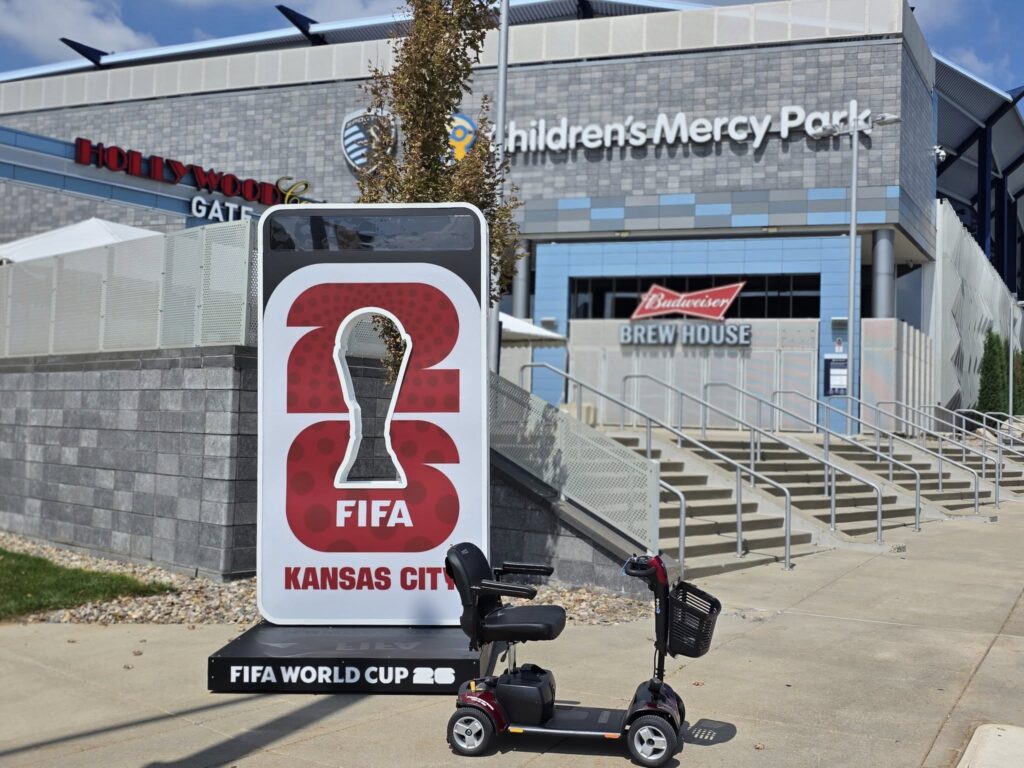 A Mobility Scooter Parked in front of a sign with the countdown to world cup 2026 in Kansas City. Children's Mercy Park, home of Sporting KC soccer team is in the Background